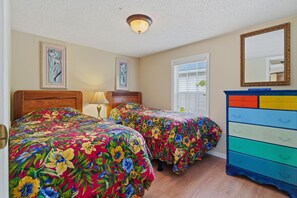 A bedroom with two beds, a dresser, and a ceiling light.