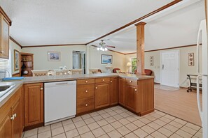A kitchen with wooden cabinets, a dishwasher, a ceiling fan, and a dining area with chairs and a table. - Coastal Escape Minutes from Cherry Grove! (North Myrtle Beach)