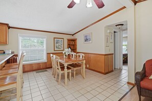 Uma sala de jantar com mesa e cadeiras de madeira, uma cozinha com armários de madeira e um corredor que leva a outro quarto.