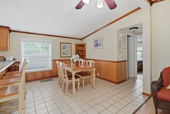 A dining area with a wooden table and chairs, a kitchen with wooden cabinets, and a hallway leading to another room.
