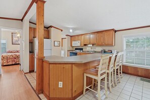 A kitchen with wooden cabinets, a central island with bar stools, a microwave, and a refrigerator. - Coastal Escape Minutes from Cherry Grove! (North Myrtle Beach)