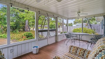 A covered patio with a wooden deck, outdoor furniture, and a view of the surrounding greenery.