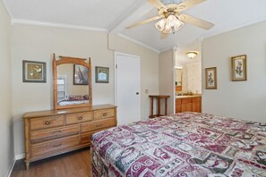 Ein Schlafzimmer mit Bett, Kommode, Spiegel, Deckenventilator und gerahmten Kunstwerken an den Wänden.