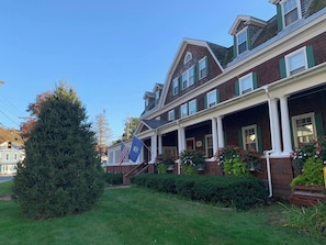 A two-story house with a front porch, green shutters, and a flag.