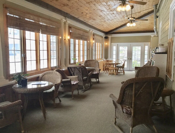 A spacious room with wicker furniture, large windows, and a ceiling fan.