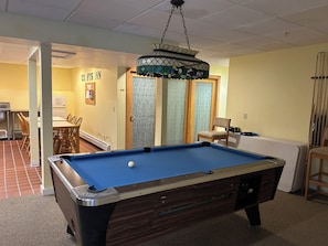 A pool table in a room with a dining area and a kitchen in the background.