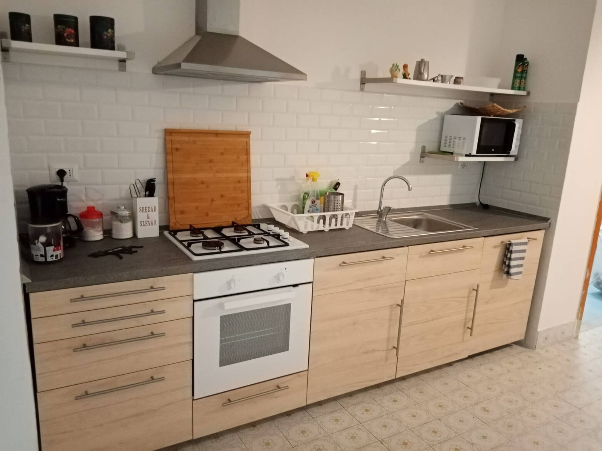 Uma cozinha moderna com fogão a gás, armários brancos, micro-ondas e uma pia de aço inoxidável.
