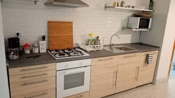 Uma cozinha moderna com fogão a gás, armários brancos, micro-ondas e uma pia de aço inoxidável.