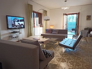 Ein Wohnzimmer mit einer Couch, einem Couchtisch, einem Fernseher und Blick ins Freie.