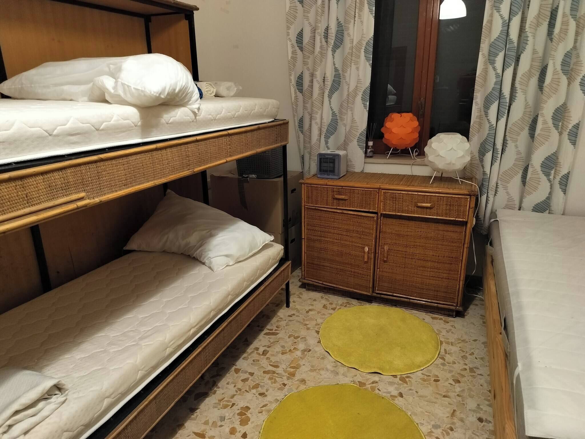 A bunk bed room with a small wooden cabinet and a window with curtains.