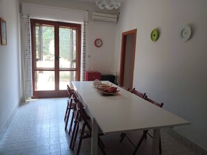 A dining area with a long table, chairs, a clock, and a door.