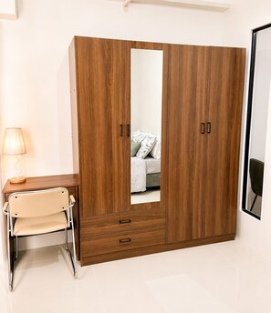 Ein Zimmer mit Holzschrank, Schreibtisch mit Stuhl und einem Bett mit Kissen.