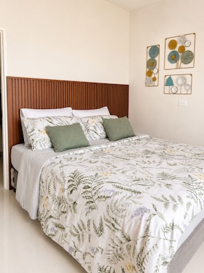 A bedroom with a wooden headboard, a floral bedspread, and wall art.