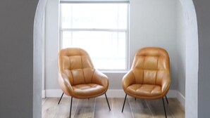 Um quarto com duas poltronas de couro, uma janela grande e piso de madeira.
