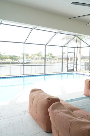 A pool area with a glass enclosure, a view of a body of water, and a seating area with a cushioned bench. - 3- Bedroom waterfront home with a pool (Punta Gorda)