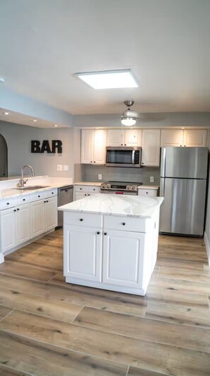 A modern kitchen with white cabinetry, a central island, a microwave, a refrigerator, and a ceiling light fixture. - 3- Bedroom waterfront home with a pool (Punta Gorda)
