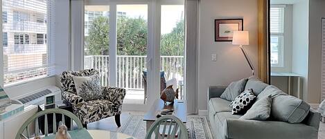 Un salon comprenant un canapé, un fauteuil, une table et un balcon offrant une vue sur les immeubles et les arbres.