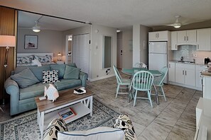 Un espace de vie compact comprenant un canapé, une table à manger avec des chaises, un coin cuisine avec des placards et un ventilateur de plafond.
