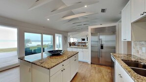 A modern kitchen with a large island, white cabinetry, and a view of the outdoors. - Ocean Sunrise | Luxury Group Retreat +  Atlantic Views (Ponte Vedra)