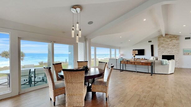A spacious dining area with a view of the ocean, a kitchen with a stone wall, and a living area with a fireplace. - Ocean Sunrise | Luxury Group Retreat +  Atlantic Views (Ponte Vedra)