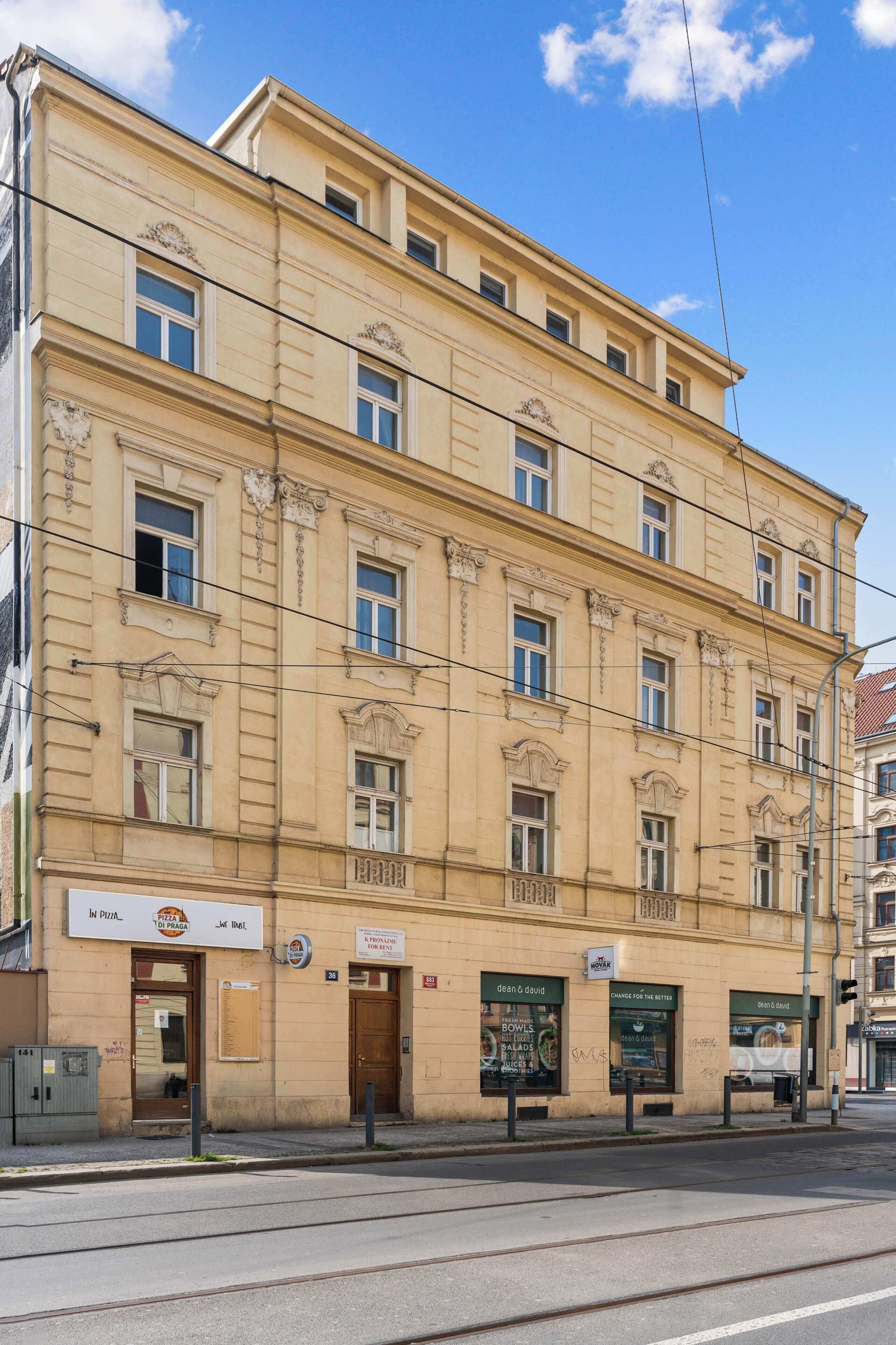 Ein mehrstöckiges Gebäude im klassischen Stil, mit einem Geschäft im Erdgeschoss und Beschilderung, einem sichtbaren Eingang und einem straßenseitigen Vordach.