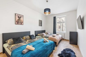 A bedroom with two beds, a large window, a flat-screen TV, and a ceiling light fixture. - Prime Chief Suite Apartworld (Praha)