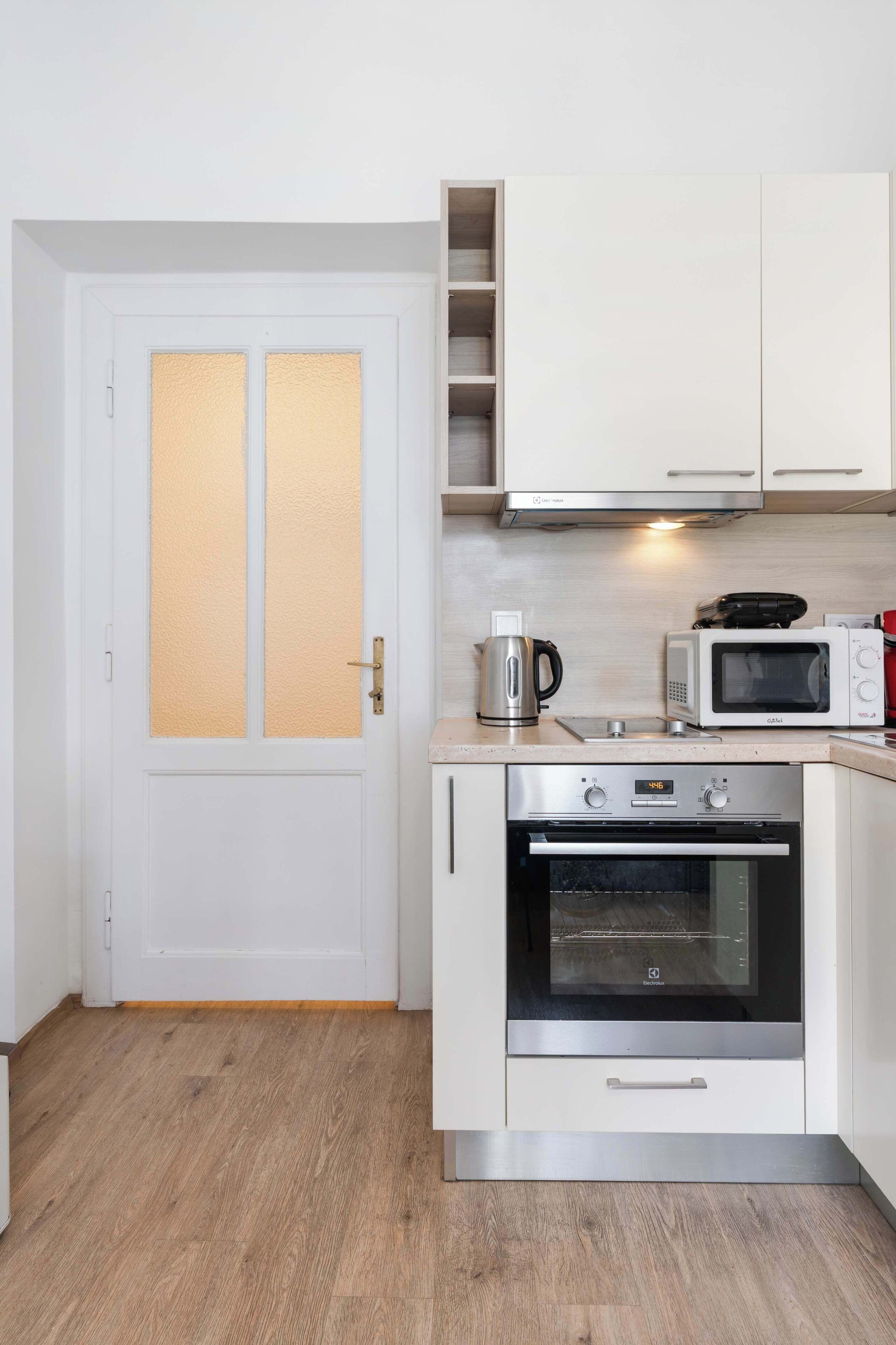 A compact kitchen with white cabinets, a microwave, an oven, and a coffee maker.