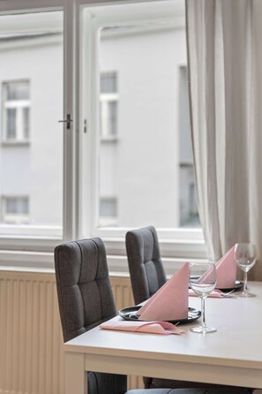 Ein Esstisch mit Stühlen, ein Fenster mit Vorhängen und Blick auf Gebäude.