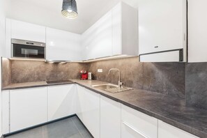 A modern kitchen with white cabinets, a stainless steel sink, a built-in oven, and a coffee machine. - Big Boss Home Apartworld (Praha)