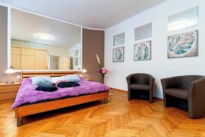 A modern bedroom with a large bed, two chairs, a mirror, and artwork on the walls. - Moonlight Deluxe Suite (Prague)