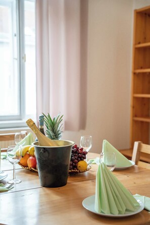 A dining table with a bottle of champagne, a pineapple, and a basket of fruits. - Old Town Suite Apartworld (Hlavní město Praha)