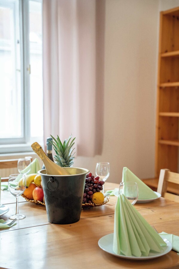 A dining table with a bottle of champagne, a pineapple, and a basket of fruits. - Old Town Suite Apartworld (Hlavní město Praha)