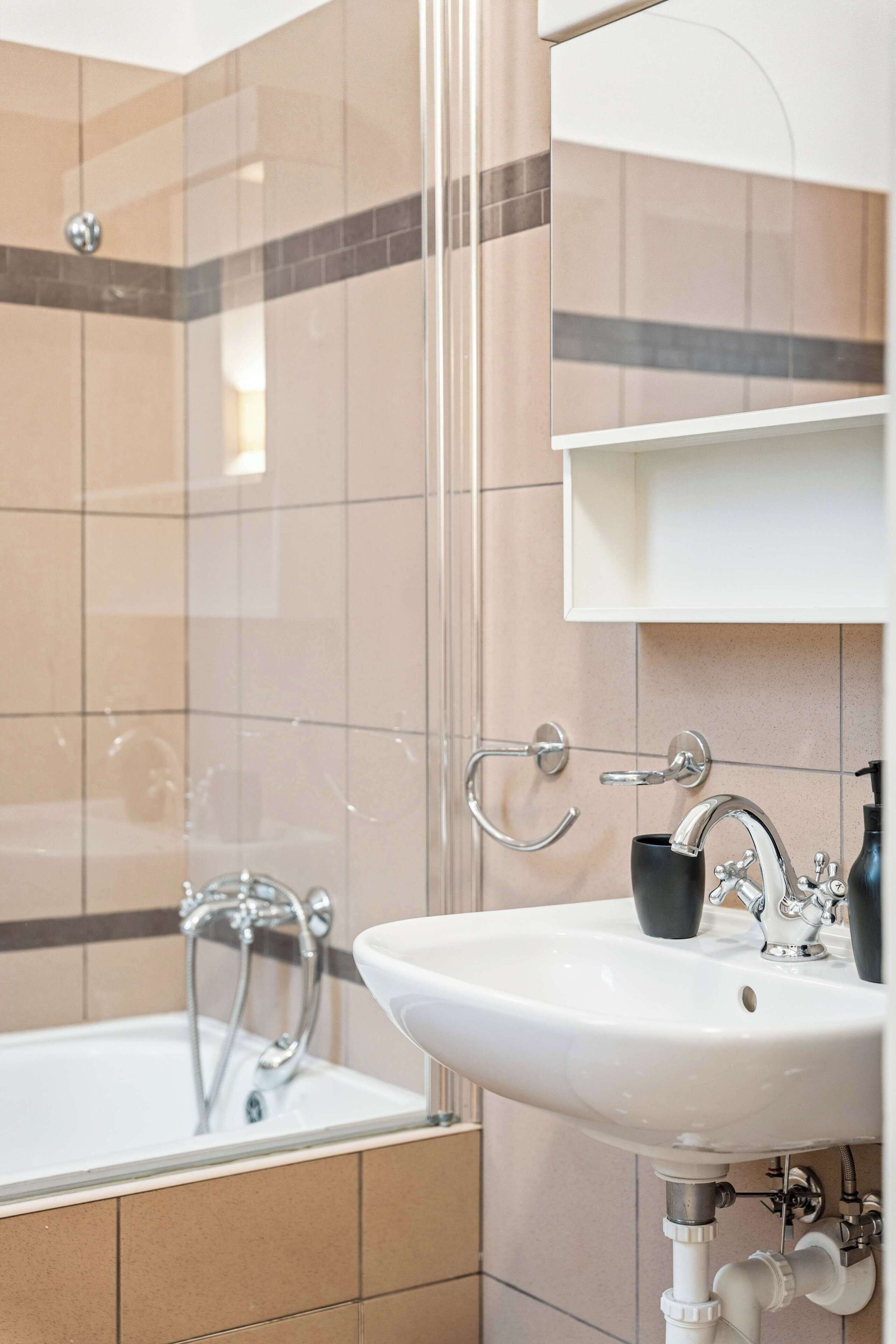 A modern bathroom with a glass shower enclosure, a white sink with chrome fixtures, and a tiled wall.