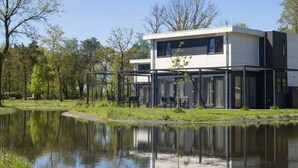 Un edificio moderno di due piani con tetto piatto, ampie finestre e il suo riflesso nell'acqua.