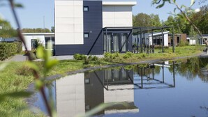 Un edificio moderno con tetto piatto, ampie finestre e il suo riflesso nell'acqua.