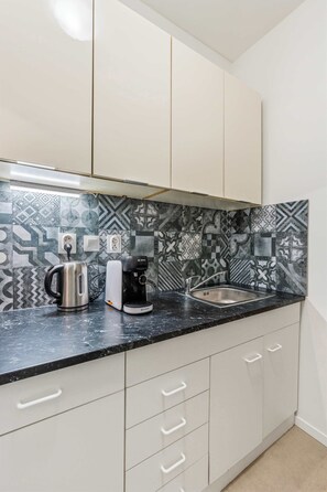A kitchen with patterned backsplash, a kettle, a coffee maker, and a sink. - Secret Courtyard Residence Apartworld (Praha)