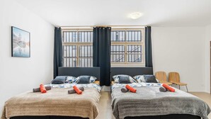 Ein Zimmer mit zwei Betten, einem vergitterten Fenster, einem Bild an der Wand und zwei Stühlen.