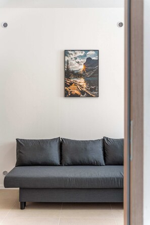 A modern living room with a grey sofa, a framed landscape painting, and a white wall. - Secret Courtyard Residence Apartworld (Praha)