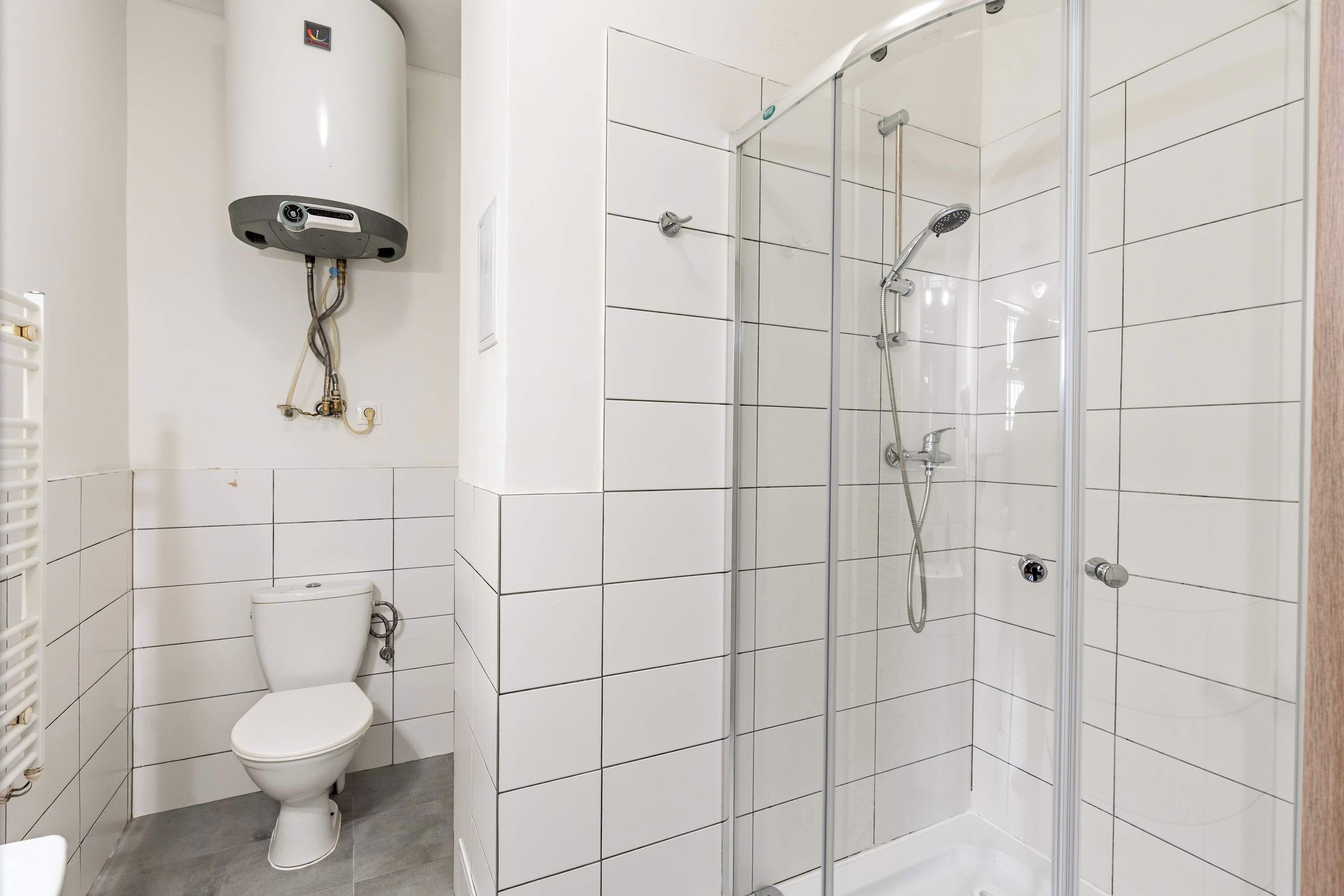 Et badeværelse med toilet, bruseniche i glas og en hvid flisegulv.