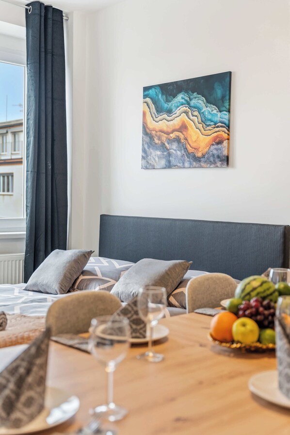 A hotel room with a bed, a dining table with fruit and glasses, and a painting on the wall.
