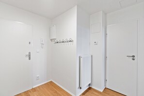 Et værelse med hvide vægge, trægulv, en radiator, et knagered og en dør med håndtag.
