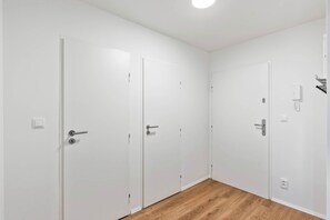 Un couloir avec des portes blanches, un interrupteur et une prise de courant sur le mur.