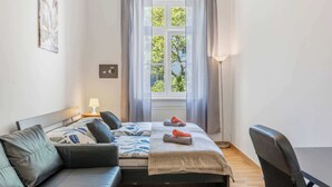 A modern bedroom with a bed, a sofa, a desk, and a window with curtains. - Historic Prague Residence Apartworld (Praha)