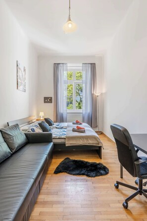 Ein modernes Schlafzimmer mit Bett, Sofa, Schreibtisch und einem Fenster mit Vorhängen.