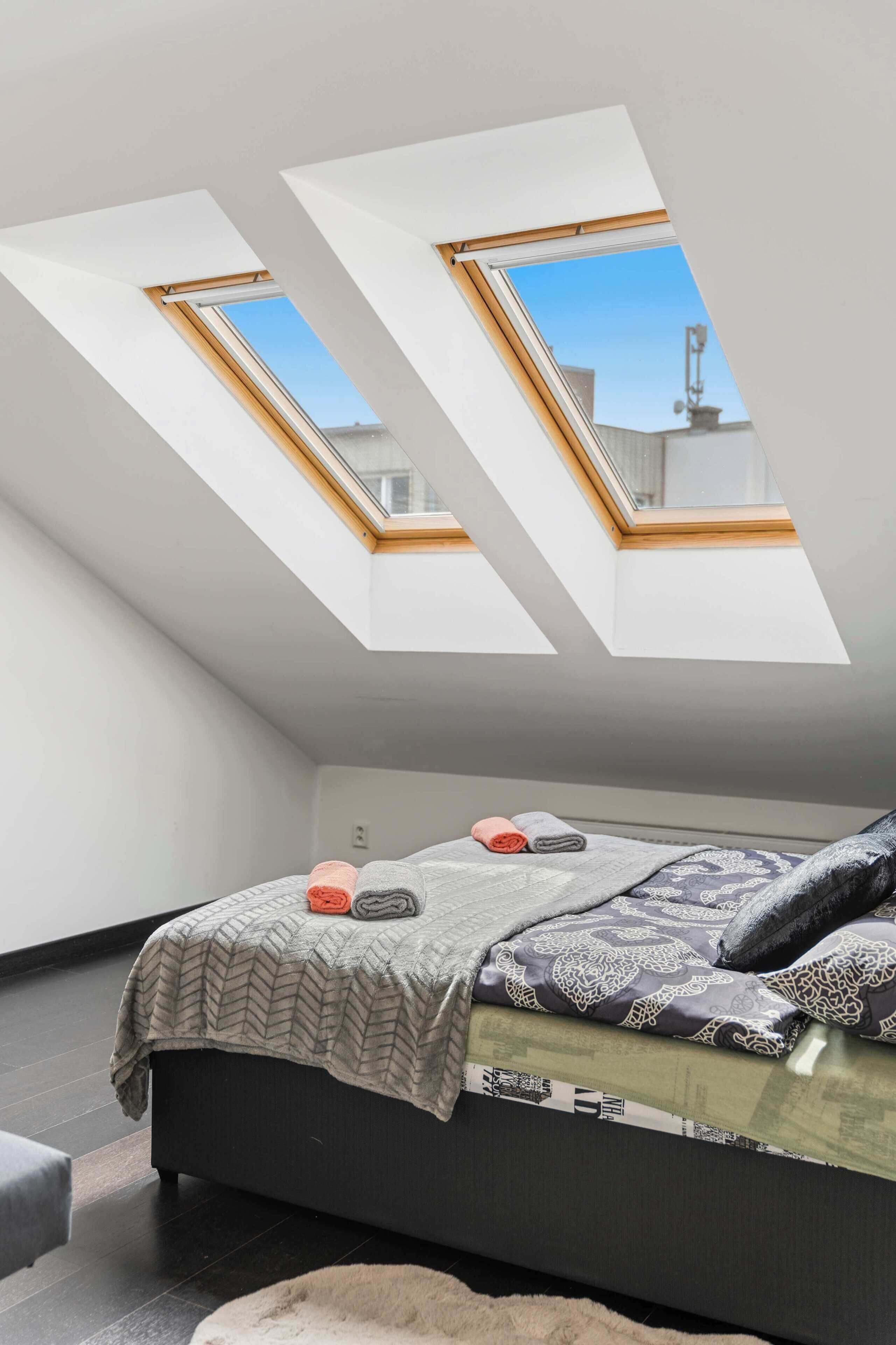 A bedroom with a skylight, a bed with patterned bedding, and a dark floor.
