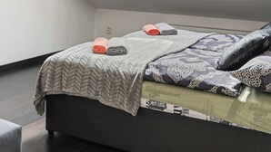 Un dormitorio con tragaluz, cama con ropa de cama estampada y suelo oscuro.
