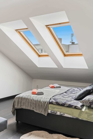 A bedroom with a skylight, a bed with patterned bedding, and a dark floor. - DiCaprio Penthouse Terrace Apartworld (Praha)
