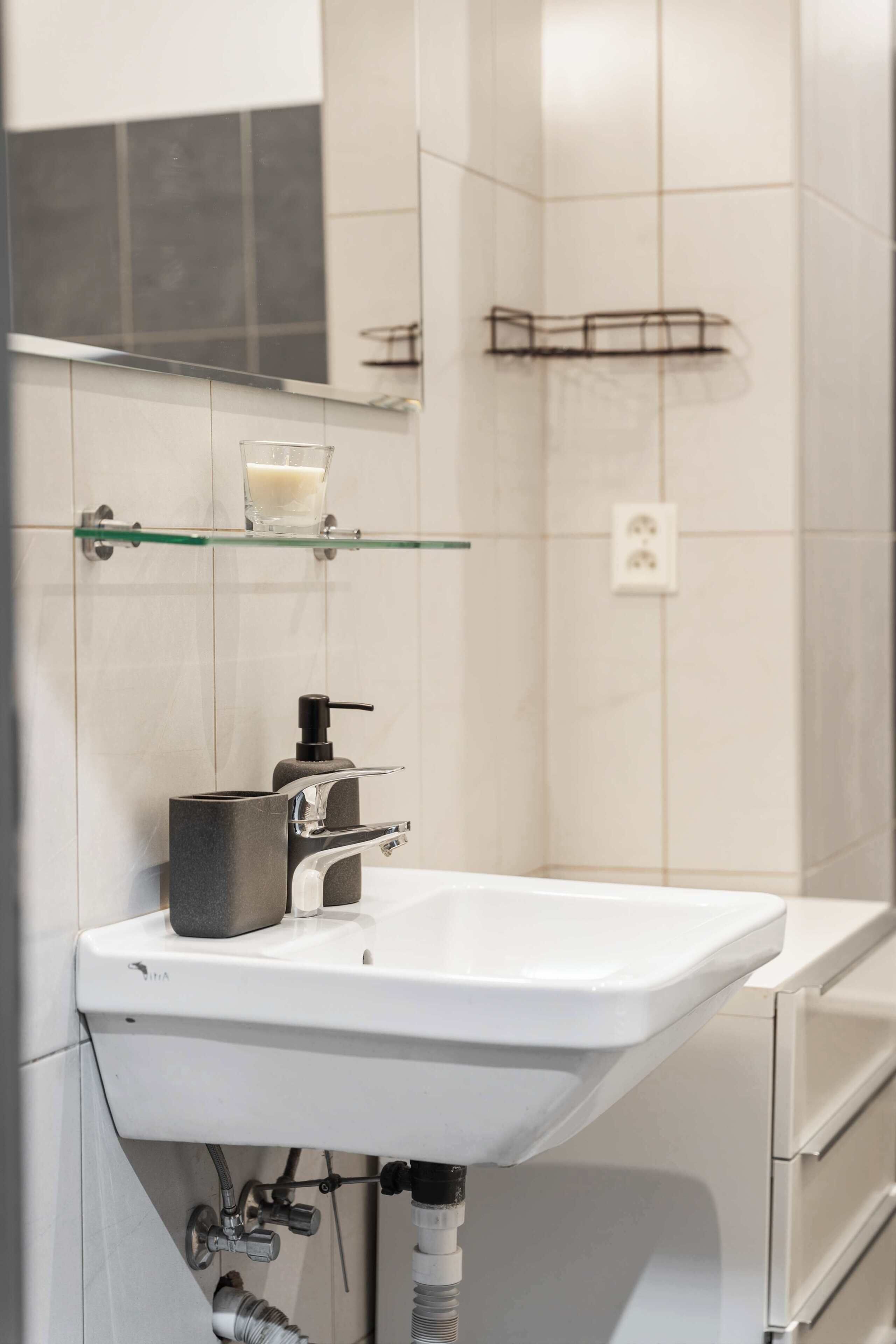 A bathroom with a white sink, a glass shelf with a soap dispenser, and a mirror above the sink.