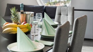 Un comedor moderno con una mesa dispuesta para dos personas, una piña, plátanos y una botella de champán.