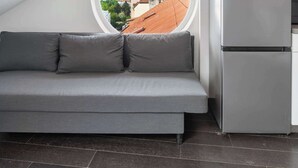 Una cocina moderna con refrigerador empotrado, un sofá gris y un ventanal circular con vistas a la ciudad.